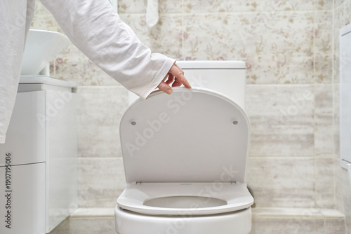 Photos Young caucasian female closing toilet lid in modern bathroom with floral wallpaper and white fixtures