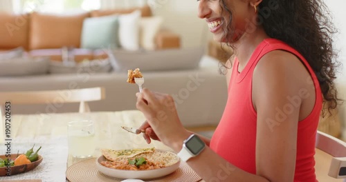 African American woman picking up fork and knife, cutting and eating meal at wooden dining table
