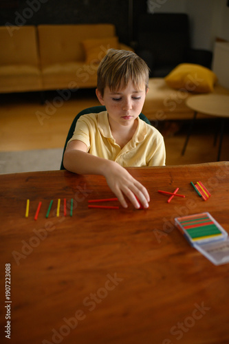 Wallpaper Mural Boy sitting at a table at home using wooden counting sticks to learn math. Child practicing basic arithmetic and number skills in a calm home learning environment. Torontodigital.ca