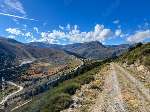 Fotografie Dirt track winding through Porte Puymorens valley under blue sky