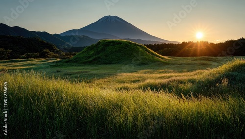 Lush green field & mound with snow-capped mountain, sun rising