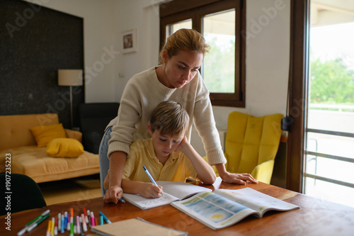 Wallpaper Mural Mother checking her son’s homework and studying lessons together at home. Warm family scene showing care, support and learning in everyday domestic life. Torontodigital.ca