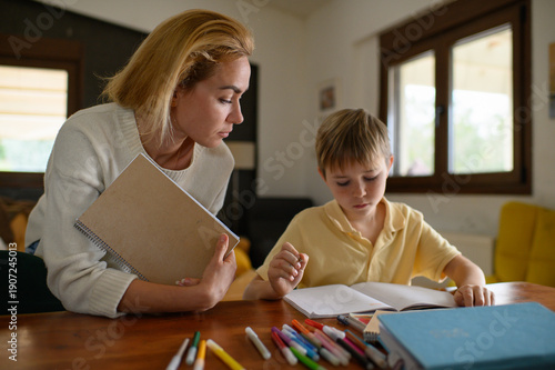 Wallpaper Mural Mother checking her son’s homework and studying lessons together at home. Warm family scene showing care, support and learning in everyday domestic life. Torontodigital.ca