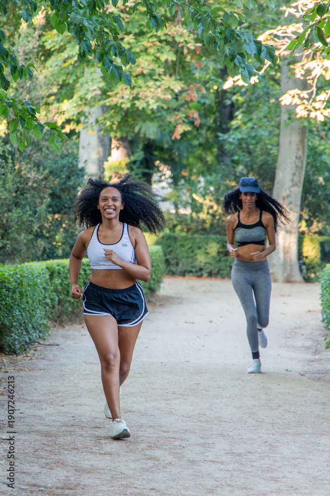 Fototapeta premium vertical Two smiling latin athletes running in a park during summer day