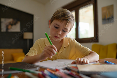 Wallpaper Mural Schoolboy sitting at a desk doing homework, writing with a marker in a workbook. Focused child studying lessons at home or in classroom. Torontodigital.ca