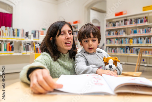 Mother and son reading book together in library