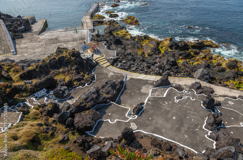 Volcanic natural swimming pools at Cinco Ribeiras on Terceira Island, Azores, Portugal. Black lava rocks, Atlantic Ocean waves and coastal bathing area under clear summer light