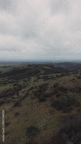 Aerial view of a countryside panorama surrounded by rolling green hills under a cloudy sky. Peaceful rural landscape, slow travel concept, outdoor activity and connection with nature.