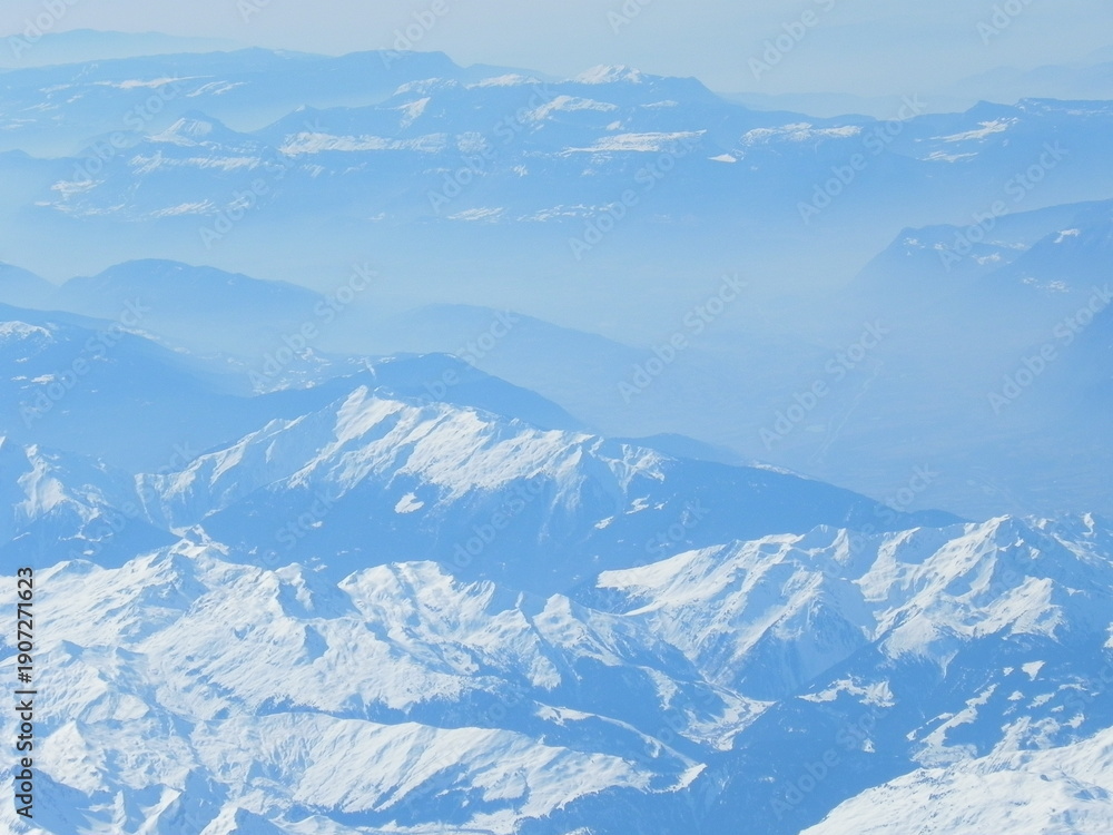 Fototapeta premium Layered snow-covered mountains fading into the distance, aerial winter landscape.