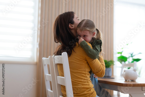 Mother comforting crying daughter with a hug at home
