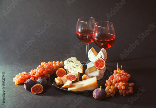 Glasses of red wine, grape, figs and various types of cheese on dark background.