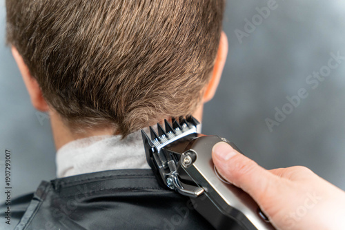 Tableau sur toile Male hairdresser using electric clippers to trim the back of a client's hair whi