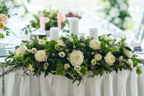 Wedding banquet table decorated with candles, flowers in elegant restaurant interior. White flower decor for wedding. Concept of celebration, romance, reception, event decoration.
