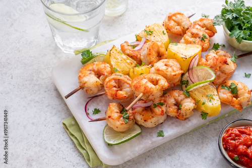 Shrimp skewers with pineapple and lime served with salsa on a white platter