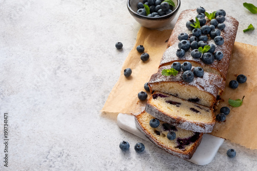 Blueberry loaf cake with slices laid out on a white plate surrounded by fresh blueberries in soft lighting