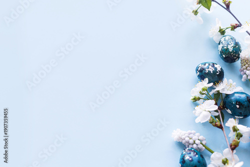 Happy Easter! Easter eggs with cherry blossom flat lay on blue background. Stylish spring template with space for text. Easter greeting card or banner