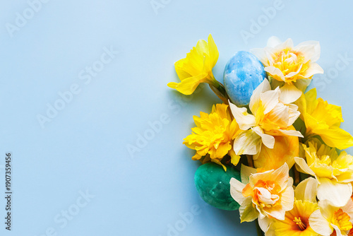 Easter flat lay. Stylish easter eggs and yellow daffodils flowers on blue background. Easter celebration, season greetings mock up. Spring  modern floral banner