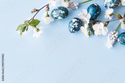 Happy Easter! Easter eggs with cherry blossom flat lay on blue background. Stylish spring template with space for text. Easter greeting card or banner