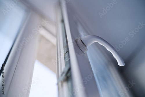 Detail of a white PVC window handle mechanism. Modern double glazing frame opened slightly for ventilation. Interior hardware fittings and home renovation. Photo