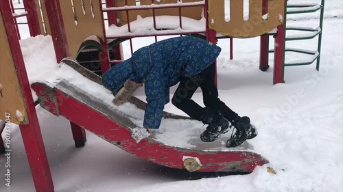 A teenage boy slides down a snow slide at a playground