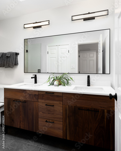Konstfotografi A modern bathroom vanity features a dark wood double sink cabinet with white countertops and black fixtures, illuminated by two linear wall lights