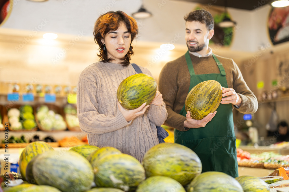 Fototapeta premium Polite young male seller offering melon to girl standing by product stand in grocery store