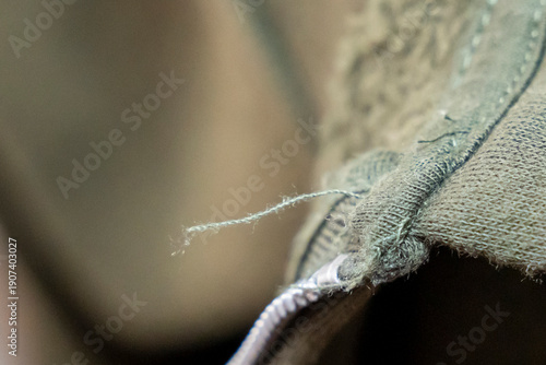 Close-up of a frayed edge on a fabric item displaying stitching details. Ideal for textiles, sewing, crafts, or fashion contexts, emphasizing fabric quality and repair.