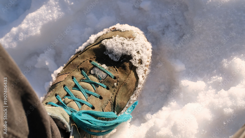 Obraz premium Worn hiking boot with teal laces partially covered in snow on sunlit winter ground
