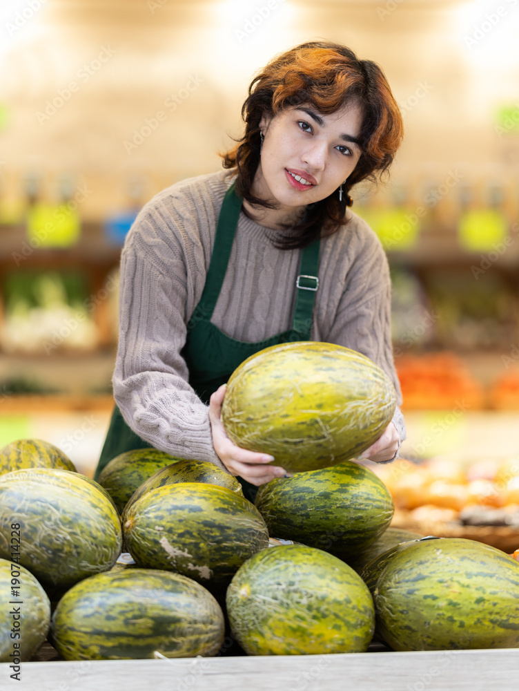 Fototapeta premium Woman employees in uniform holding fresh pumpkin in grocery shop