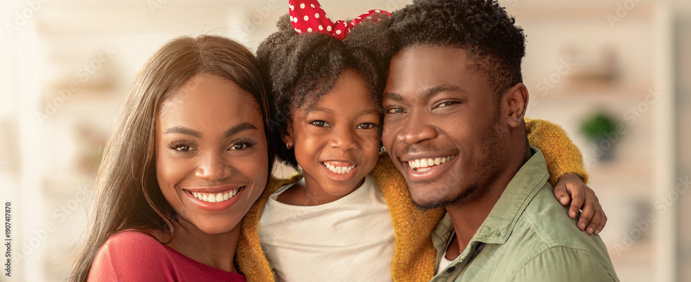 Obraz premium Family stands together in a bright living room. The parents smile widely, while the child in the middle beams with joy. This moment captures their love and togetherness.