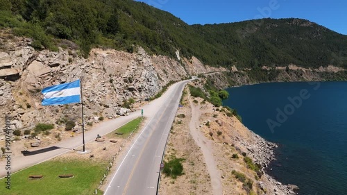 Argentine flag waving proudly over a scenic mountain road in San Martin de los Andes, Neuquen, Patagonia, representing national pride, federalism, and the spirit of the Argentine Republic.