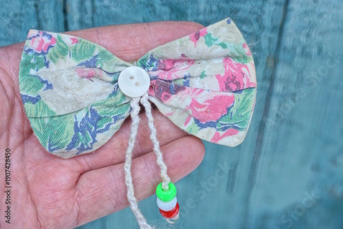  hand holds of clothing made of one color fabric bow tie with a white button in green background