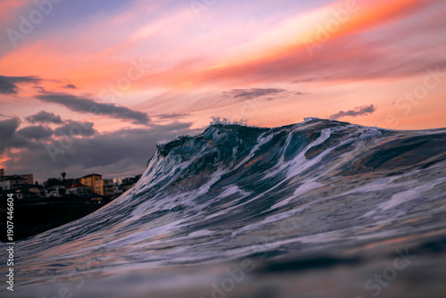 A breaking ocean wave at sunset at Bronte Beach, Sydney, Australia, with soft pink clouds and fading light reflecting across the water.