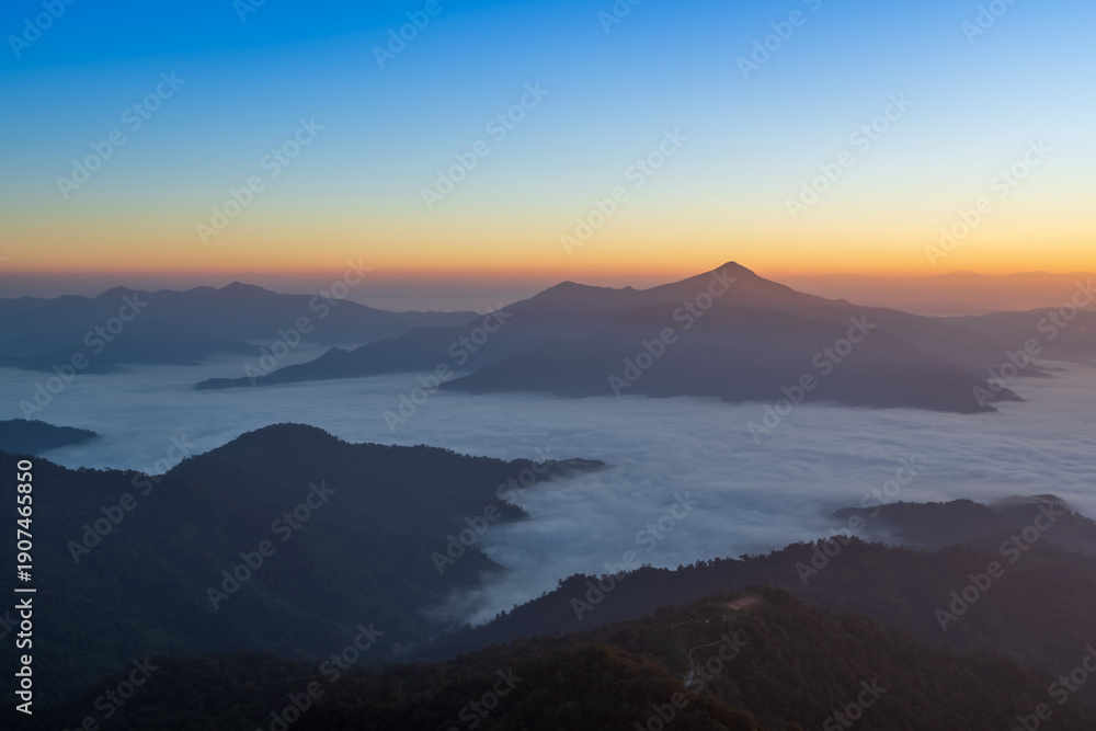Fototapeta premium Soft sunrise light over misty mountains and layered horizon.