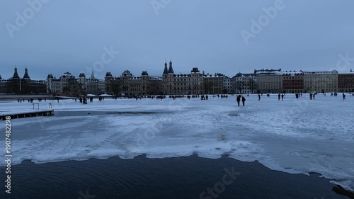 A view across a frozen canal of people on the ice. Many people walk on the ice. The capital of Denmark