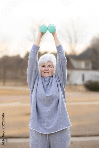 Active senior woman lifting dumbbells during outdoor workout
