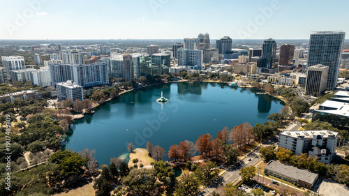 A sweeping drone view of Lake Eola Park highlights the downtown Orlando skyline reflected across the lake.