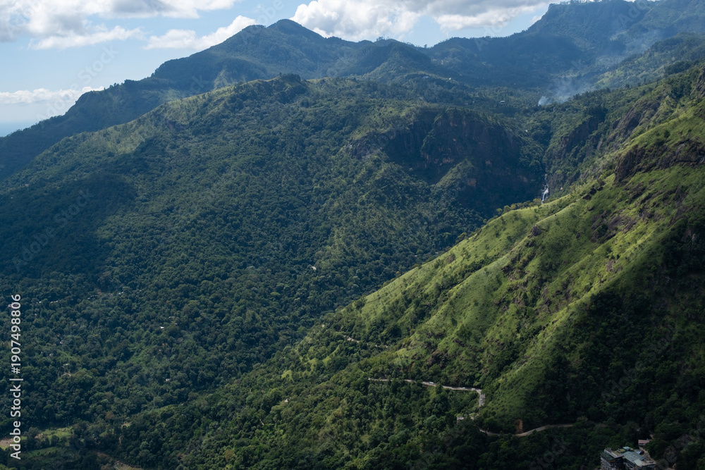 Obraz premium Winding mountain road on the slope of Ella Rock, Sri Lanka, seen from Little Adam’s Peak. Lush greenery, scenic depth and tropical highland landscape create an inspiring travel scene.