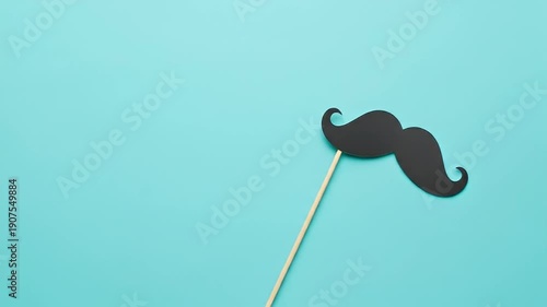 Black Mustache Prop on a Stick Against a Teal Background.