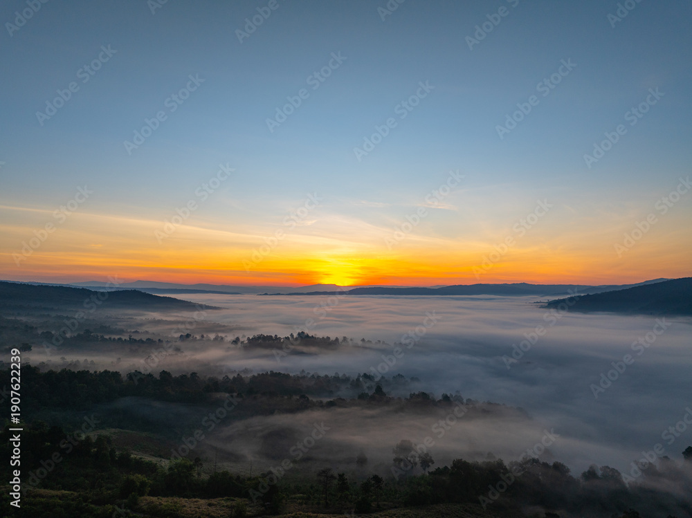 Obraz premium An aerial cinematic sunrise showcasing vibrant sky colors above a fog-covered valley, creating a serene and inspiring nature travel atmosphere. Brilliant Sunrise Painting the Sky Over the Valley