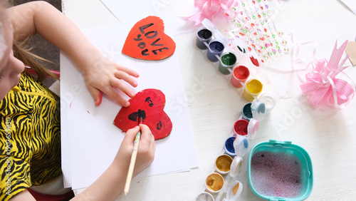 Child making homemade greeting card. A little girl paints hearts and funny pet as a gift for Mother’s Day or VAlentines day . Traditional play concept. Arts and crafts concept.