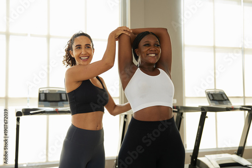 Woman is instructing her friend to do arm stretches at the gym