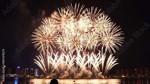 Vibrant red fireworks explode over a sparkling city skyline at night