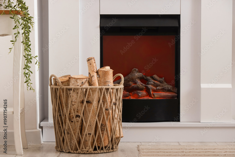 Naklejka premium Wicker basket of firewood near fireplace in living room, closeup
