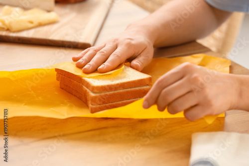 Bilde på lerret Young woman wrapping fresh bread slices in beeswax paper on table at home, close