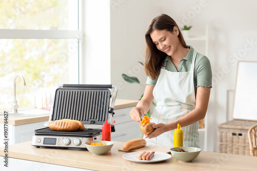 Young woman cooking hot dog with Korean carrot in kitchen