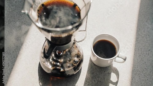 Freshly brewed dark coffee in a glass carafe and a white mug on a sunlit counter