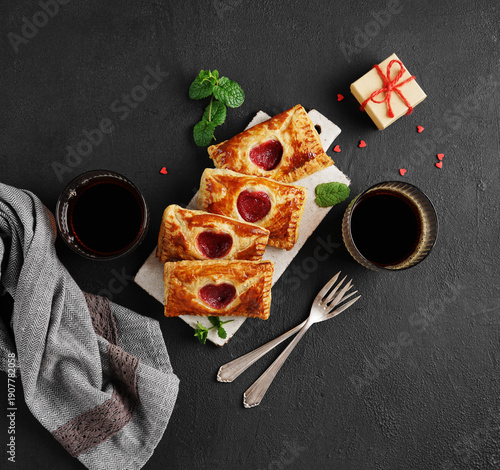 Love letter cookies on black background with two cups of coffee and a little present box. Envelopes with cherry jam filling, Dessert for Valentine day. top view
