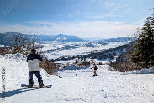 Snowboarder standing on slope overlooking snowy valley at Togari Onsen, Japan