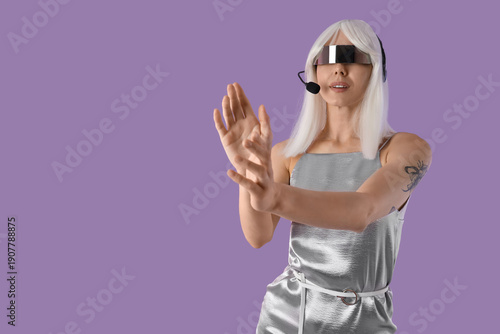 Young woman in futuristic costume with VR glasses on lilac background
